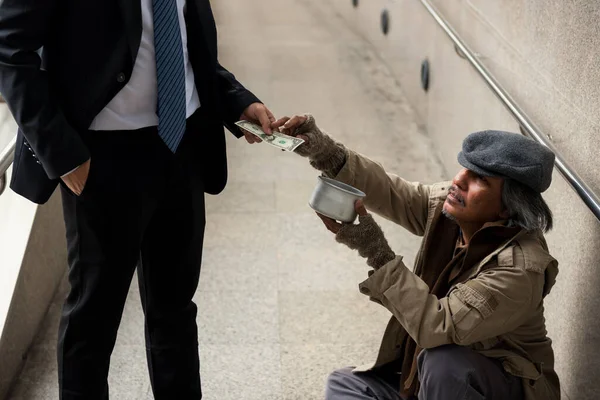年取った乞食かホームレスの人は冬の都市の町の歩く親切なビジネス人によって1ドル札のお金をつかむ 貧困と社会問題の概念 寄付して同情するのを手伝って — ストック写真