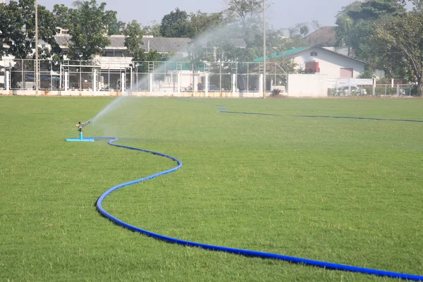 Rubber tube spraying water into soccer field — Stock Photo, Image