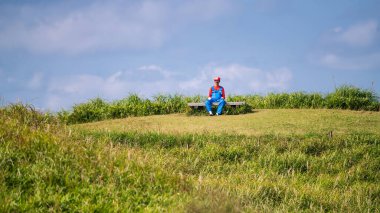 Mario üniformalı Japon adam Daikanbo Gözlemevi 'nin dağlık zirvesinde mavi gökyüzüne karşı sandalyede oturuyor. Ünlü anime oyun karakteri, Kumamoto, Japonya