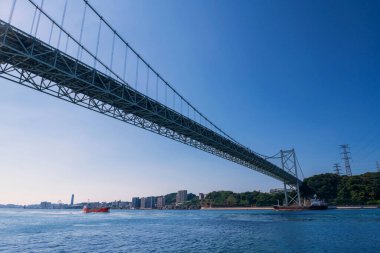 Kanmon Köprüsü 'nden geçen kargo gemileri mavi gökyüzüne, Kitakyushu' ya, Fukuoka 'ya, Japonya' ya karşı. Asma köprü Kyushu ve Honshu adasını geçiyor. Lojistik endüstrisi.