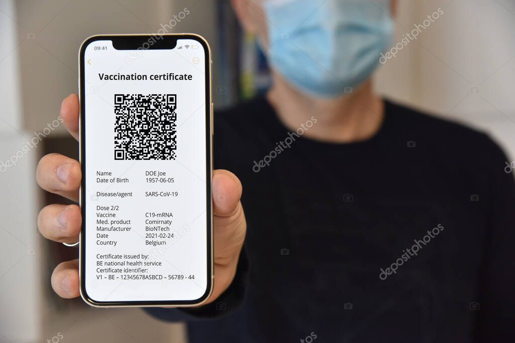 Man with face mask holding mobile phone with digital green certificate of vaccination against Covid-19, a negative PCR test or recovery from Covid-19. Travel concept during coronavirus pandemic.