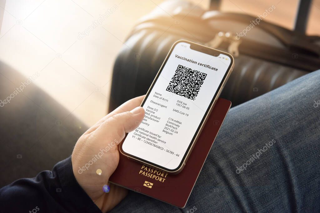 Digital certificate of vaccination against Covid-19. A man holds a passport and a mobile phone next to a travel bag. Travel concept during coronavirus pandemic.