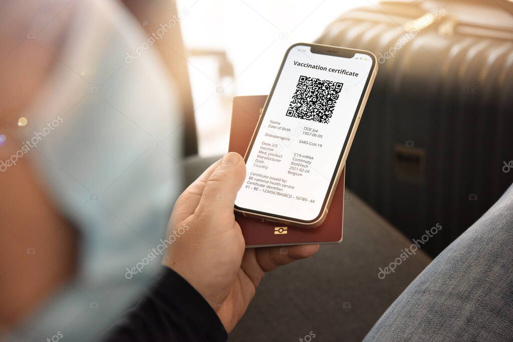 Man with face mask holding smartphone with digital certificate of vaccination against Covid-19 and passport. Travel and tourism concept during coronavirus pandemic.