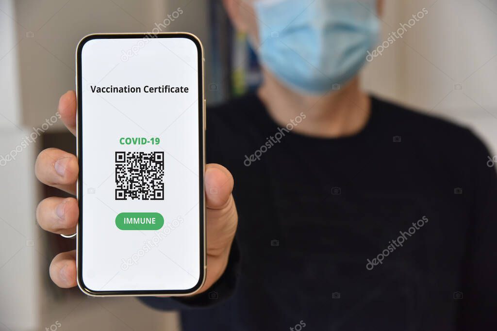 Digital certificate of vaccination against Covid-19. Man with face mask holding mobile phone with digital certificate of vaccination against Covid-19, a negative PCR test or recovery from coronavirus.