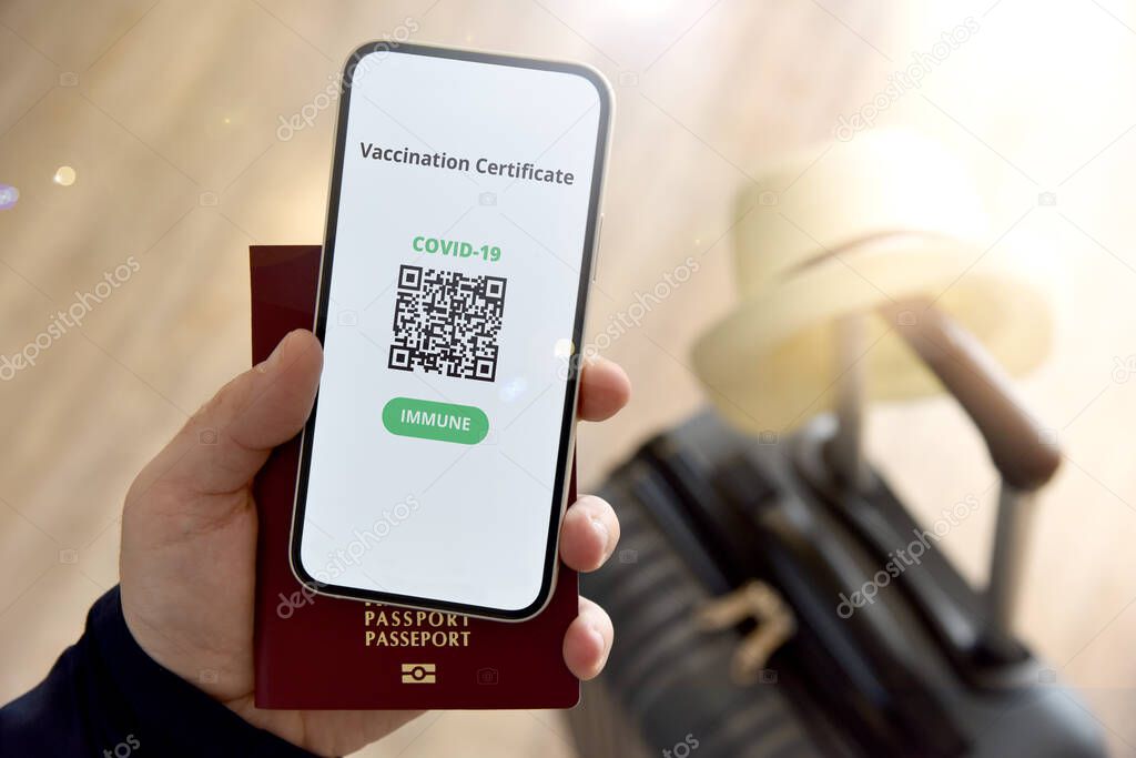 Digital certificate of vaccination against Covid-19. A man holds a passport and a mobile phone next to a travel bag. Travel concept during coronavirus pandemic.