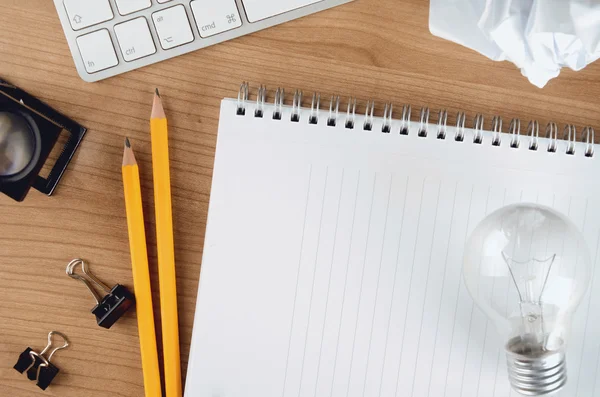 Desktop concept with paper, stationery, computer, blank notepad and light bulb, top view — Stock Fotó