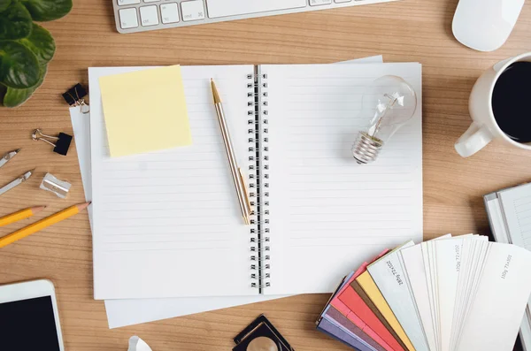 Lugar de trabajo creativo con bloc de notas, equipo de diseño, teléfono inteligente, bombilla, computadora y etiqueta engomada en blanco — Foto de Stock