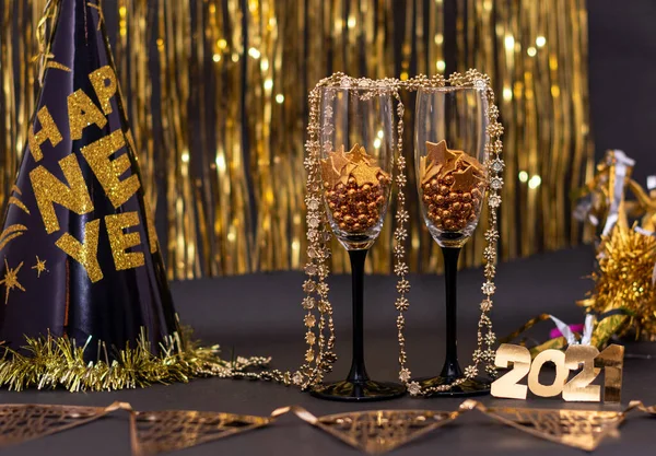 2021年は 金色の数字 新年の帽子 黒と金色の背景のバナーから作られた小さな黄金のボールと星を持つ2つのワイングラス お正月飾り — ストック写真