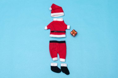 Süveter, pantolon, bot ve şapka, Noel Baba giysileri ve mavi arka planda küçük kırmızı bir hediye.