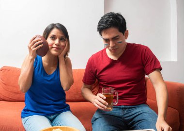 Kanepede oturan Latin çift, bir Amerikan futbol maçı sırasında üzgündü.. 