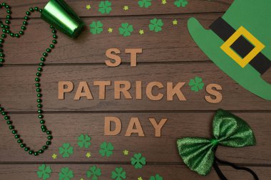 Düz fotoğraf çekimi. Ahşap harflerden, yeşil bardaktan, yonca konfetisinden, leprikon şapkadan ve ahşap arka planda yeşil fiyonktan yapılmış Aziz Patrick Günü.