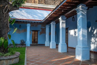 CUERNAVACA, MORELOS, MEKSİKO- 20 Şubat 2026 Cuernavaca, Morelos 'taki tarihi Jardin Borda' da klasik bir koloni avlusunun huzurlu manzarası. Sahnede parlak açık mavi duvarlar, sağlam beyaz sütunlar ve kırmızı bir terracotta fayans zemin düzenlemesi yer alıyor.