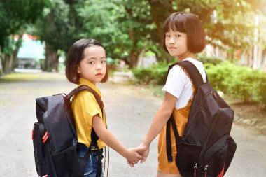 İlkokulun iki öğrencisi el ele tutuşuyor. Okul çantaları arkasında olan kız çocuğu. Okula geri dön..
