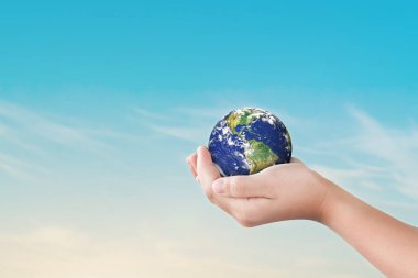 Çevre günü konsepti, Globe in children hands over blue sky background. Dünya 'nın kurtuluşu. Bu görüntünün elementleri NASA tarafından desteklenmektedir