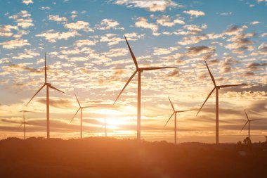 Rüzgar türbini günbatımında gökyüzü arka planında elektrik üretir.