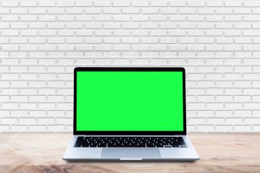 Beyaz tuğla duvar arkaplanı olan ahşap masadaki boş yeşil ekran..