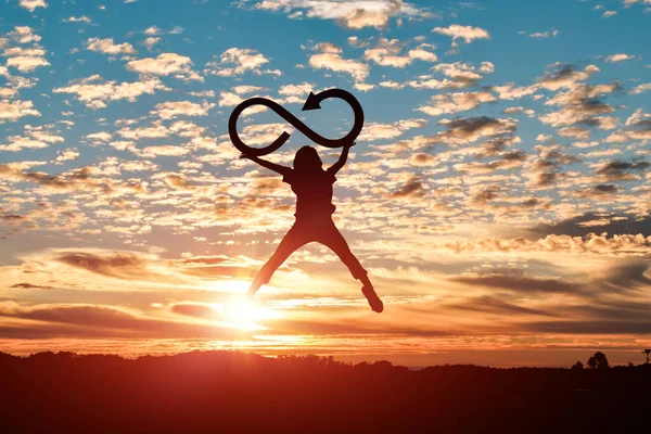 女性のシルエットジャンプし 日没の背景に無限のシンボルを保持しています — ストック写真
