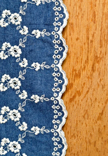 Tessuto jeans con ricamo di fiori bianchi posato sopra il bacc di compensato — Foto Stock