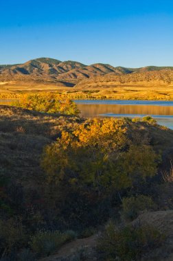 Sabah güneşinin sıcacık parıltısı sonbahar ağaçlarının tepesini ve soğuk bir ekim sabahı Colorado 'daki Chatfield Gölü' nde uzak dağları yıkıyor..