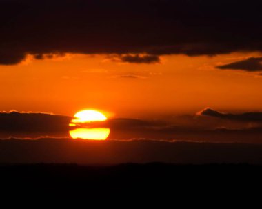 The sun slips behind clouds as the sky glows orange.