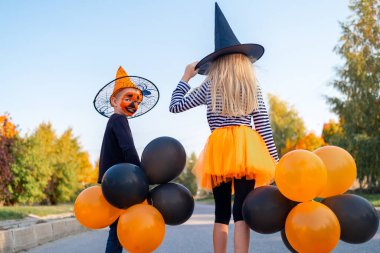 Cadılar Bayramı çocukları. Cadılar Bayramı 'nı dışarıda kutlayan karnaval kostümlü kardeşlerimiz. Cadı şapkalı, balkabağı kovalı kız ve erkek. Turuncu ve siyah balonları olan komik çocuklar.. 