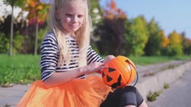 4 bin. Cadılar Bayramı çocukları. Şiddetli rüzgârdan dolayı şapkası koptu. Elinde balkabağı kovası olan cadı kostümlü sarışın kız. Çocuk dışarıda şeker yiyor.. 