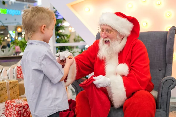 Jultomten pratar och leker överraskningslekar med barn i shoppingcentret. Julförsäljning och önskemål — Stockfoto