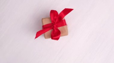Pembe ahşap arka planda dönen kırmızı kurdeleli hediye kutusu. 360 derece dönüş. Kusursuz döngü. Konsept satışlar, indirimli fiyatlar, Noel tatilleri ve alışveriş.