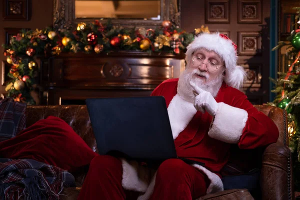 Boże Narodzenie online gratulacje od Mikołaja. Święty Mikołaj za pomocą laptopa notebooka na odległość dzieci Christmas call siedzi w pobliżu choinki w domu. Szczęśliwego Nowego Roku Covid 2021 — Zdjęcie stockowe