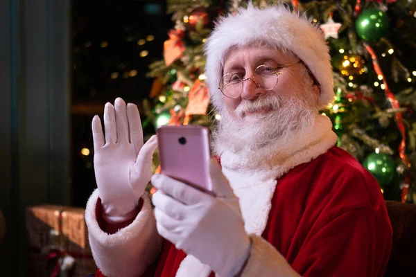 Weihnachten Online Glückwünsche vom Weihnachtsmann. Der Weihnachtsmann ruft mit dem Handy Menschen und Kinder an. Zu Hause in der Nähe des Weihnachtsbaums sitzen. Frohes neues Jahr Covid 2021 — Stockfoto