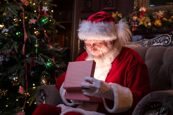 Leende jultomten öppnar julklapp. Uppfyllande av önskningar. Tomten sitter hemma nära julgranen — Stockfoto