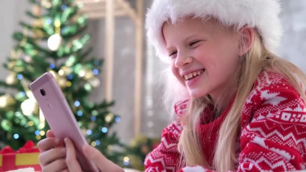 4k Weihnachten online Glückwunsch. Lächelndes Mädchen mit Handy für Videoanrufe. Kind redet mit Freunden und Eltern — Stockvideo