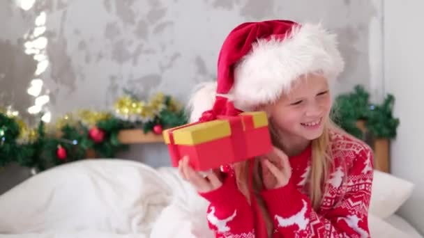4k mała dziewczynka trzęsie pudełko, aby dowiedzieć się, co jest w środku. Spełnianie życzeń, marzeń i niespodzianek świątecznych dla dzieci — Wideo stockowe
