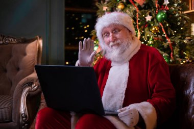 Noel Baba 'dan online tebrik. Noel Baba evde Noel ağacının yanında oturan çocukları aramak için dizüstü bilgisayar kullanıyor. Mutlu yıllar, 2021.