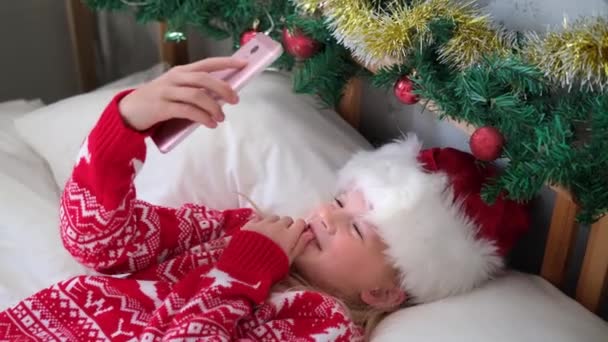 4k Boże Narodzenie online gratulacje. Uśmiechnięta dziewczyna używająca telefonu komórkowego do rozmów wideo. Dziecko mówiące przyjaciele i rodzice — Wideo stockowe