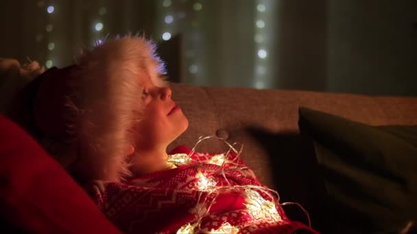 Portrait garçon rêveur dans le chapeau de Père Noël et costume de Noël assis à la maison. Nouvel An et fêtes. Fille heureuse et détendue. Remplir les souhaits, les rêves et les surprises des enfants. — Video