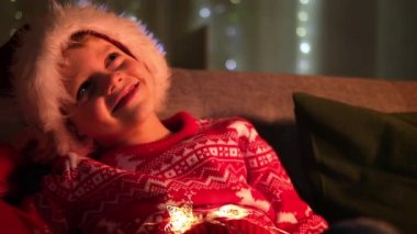 Noel Baba şapkalı ve Noel kostümlü hayalperest çocuk evde oturuyor. Yeni yıl ve tatiller. Rahatlamış mutlu çocuk. Çocukların Noel dileklerini, hayallerini ve sürprizlerini gerçekleştiriyor..