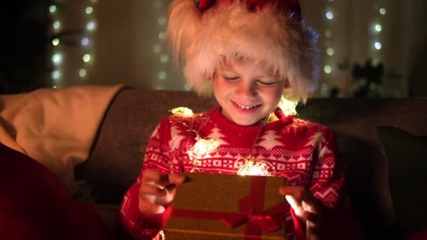 Milagre de crianças de Natal. Menino de chapéu de Papai Noel abre presente em casa. Cumprindo crianças desejos de Natal, sonhos e surpresas. — Vídeo de Stock