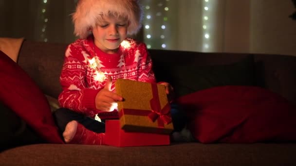 Les enfants de Noël miracle. Boy in Santa Claus chapeau ouvre cadeau à la maison. Remplir les souhaits, les rêves et les surprises des enfants. — Video