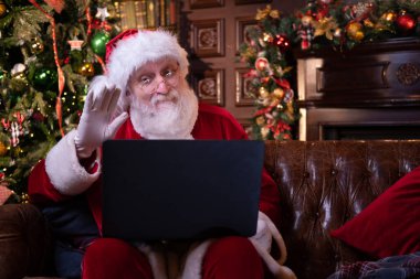 Noel Baba 'dan online tebrik. Noel Baba evde Noel ağacının yanında oturan çocukları aramak için dizüstü bilgisayar kullanıyor. Mutlu yıllar, 2021.