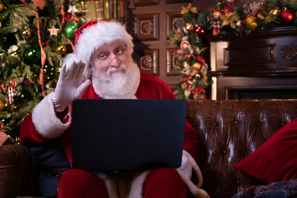 Noel Baba 'dan online tebrik. Noel Baba evde Noel ağacının yanında oturan çocukları aramak için dizüstü bilgisayar kullanıyor. Mutlu yıllar, 2021.