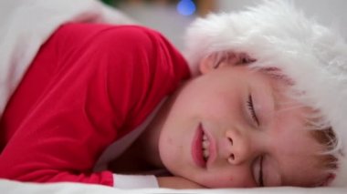 Çocuk Noel 'den önce uyuyor. Noel Baba şapkalı ve Noel pijamalı küçük çocuk beyaz yatakta yatıyor. Yeni yıl ve tatiller. sabah mutluluğu.