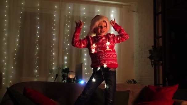 Garçon de Noël excité dansant dans le chapeau de Père Noël à la maison soir. Nouvel An et fêtes. Bonheur de Noël. — Video