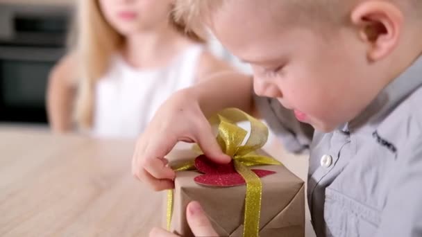 Kleiner Junge bereitet sich darauf vor, sein geliebtes Mädchen zum Valentinstag zu beschenken. Kind dekoriert Geschenkbox mit großem roten Herz. Zeitlupe. — Stockvideo