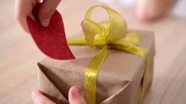 Küçük çocuk sevgilisine Sevgililer Günü hediyesi vermeye hazırlanıyor. Çocuk hediye kutusunu büyük kırmızı bir kalple süslüyor. Yavaş çekim.