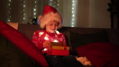 Noel çocukları mucizesi. Noel Baba şapkalı çocuk evde hediye açıyor. Çocukların Noel dileklerini, hayallerini ve sürprizlerini gerçekleştiriyor..