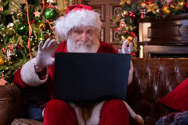 Julen online grattis från Santa. Jultomten använder bärbar dator för avstånd jul samtal barn sitter nära julgran hemma. Gott nytt år Covid 2021 — Stockfoto