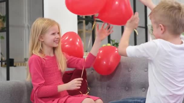 Menino e menina se divertindo brincando com balões em forma de coração vermelho em casa. A celebrar o Dia dos Namorados. Movimento lento. — Vídeo de Stock