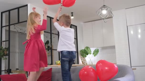 Mały chłopiec i dziewczynka tańczący z czerwonym kształcie serca balony w domu. Świętujemy Walentynki. Zwolniony ruch. — Wideo stockowe