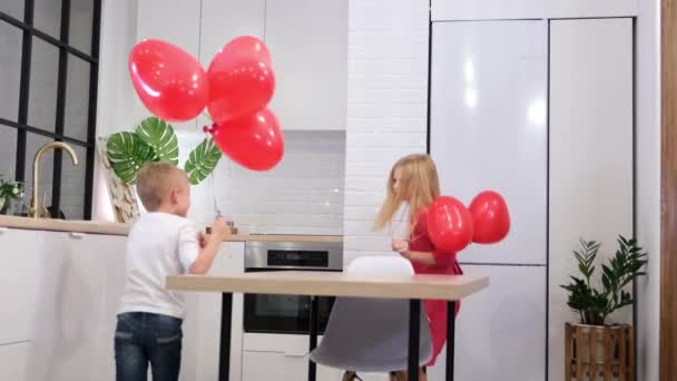 Παιδιά τρέχουν γύρω από το τραπέζι με μπαλόνια σε σχήμα κόκκινης καρδιάς στο σπίτι. Γιορτάζουμε την ημέρα του Αγίου Βαλεντίνου. Αργή κίνηση. — Αρχείο Βίντεο
